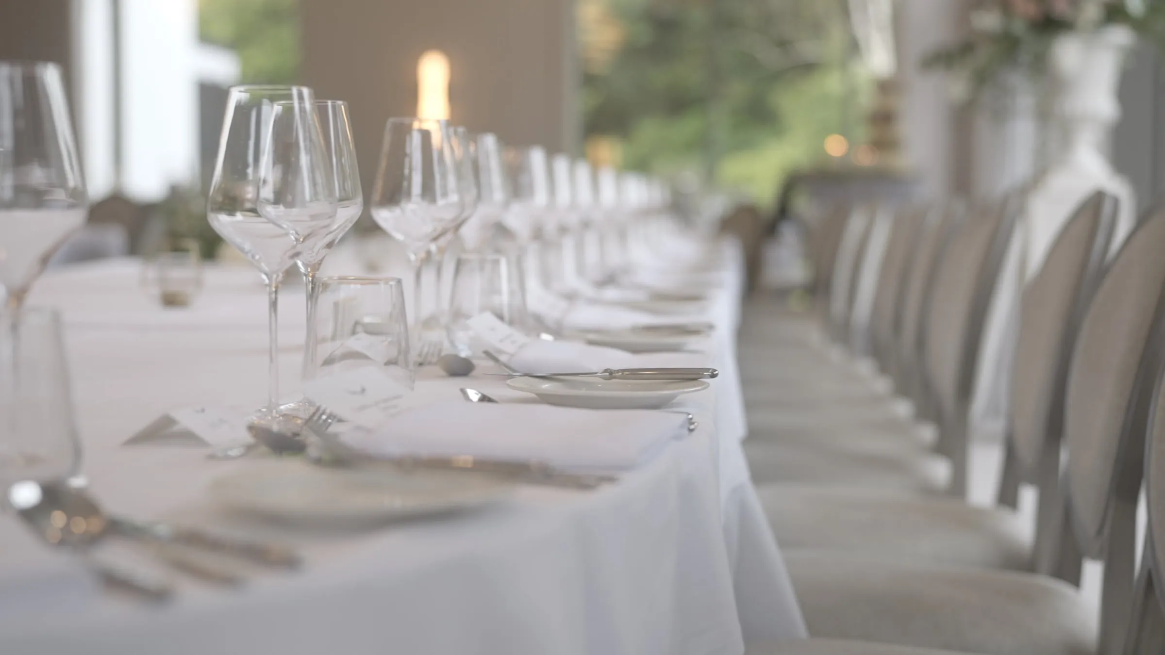 A long wedding reception table at The Grace set with glassware and white linen, beside tall windows looking out onto greenery.